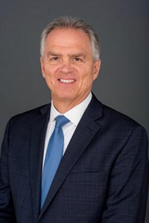 Portrait of Trustee Haber wearing a dark blue suit, white shirt and medium blue tie against a gray background