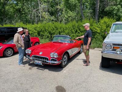 Two men and a women looking at a red vintage car at a car show.
